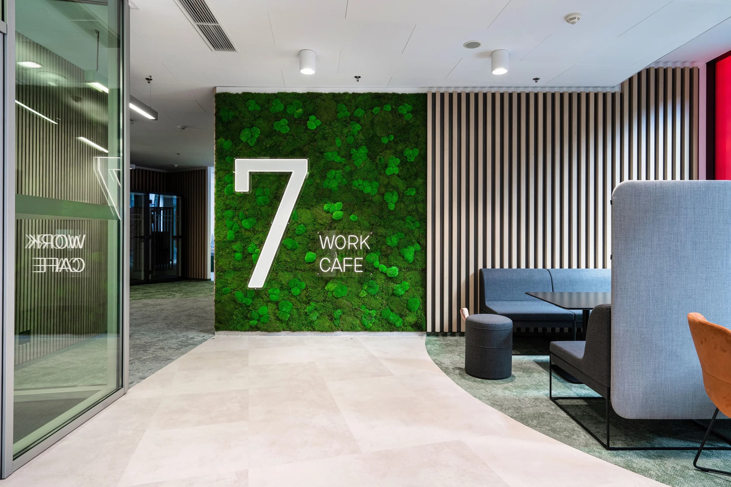 Mechová stěna s nápisem 7 Work Cafe v kanceláři Kooperativy v Praze a šedé sezení s vysokým opěradlem