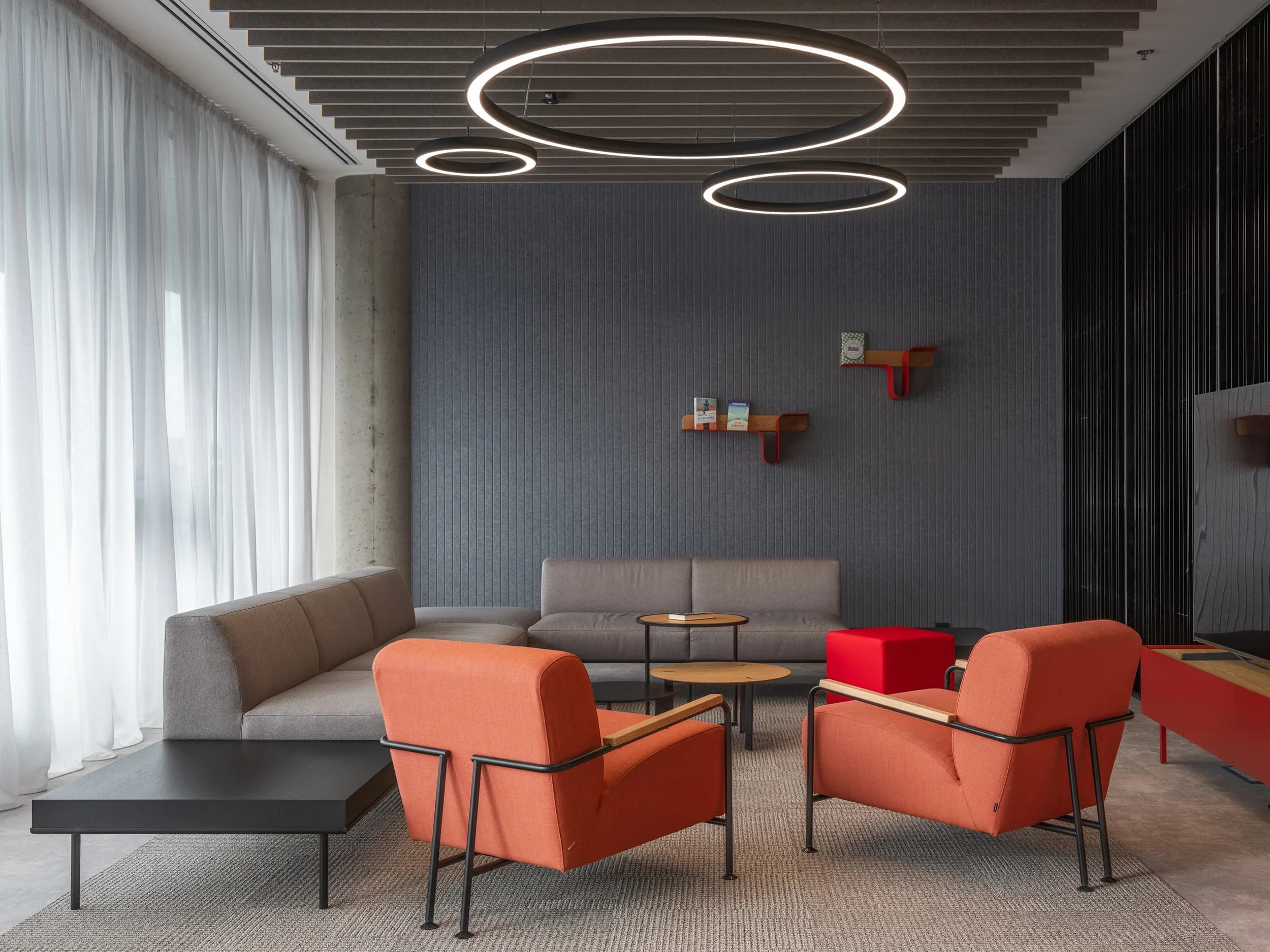 Lounge v kanceláři CLA Czech Republic v Praze s oranžovými křesly, šedou sedačkou a kruhovými svítidly