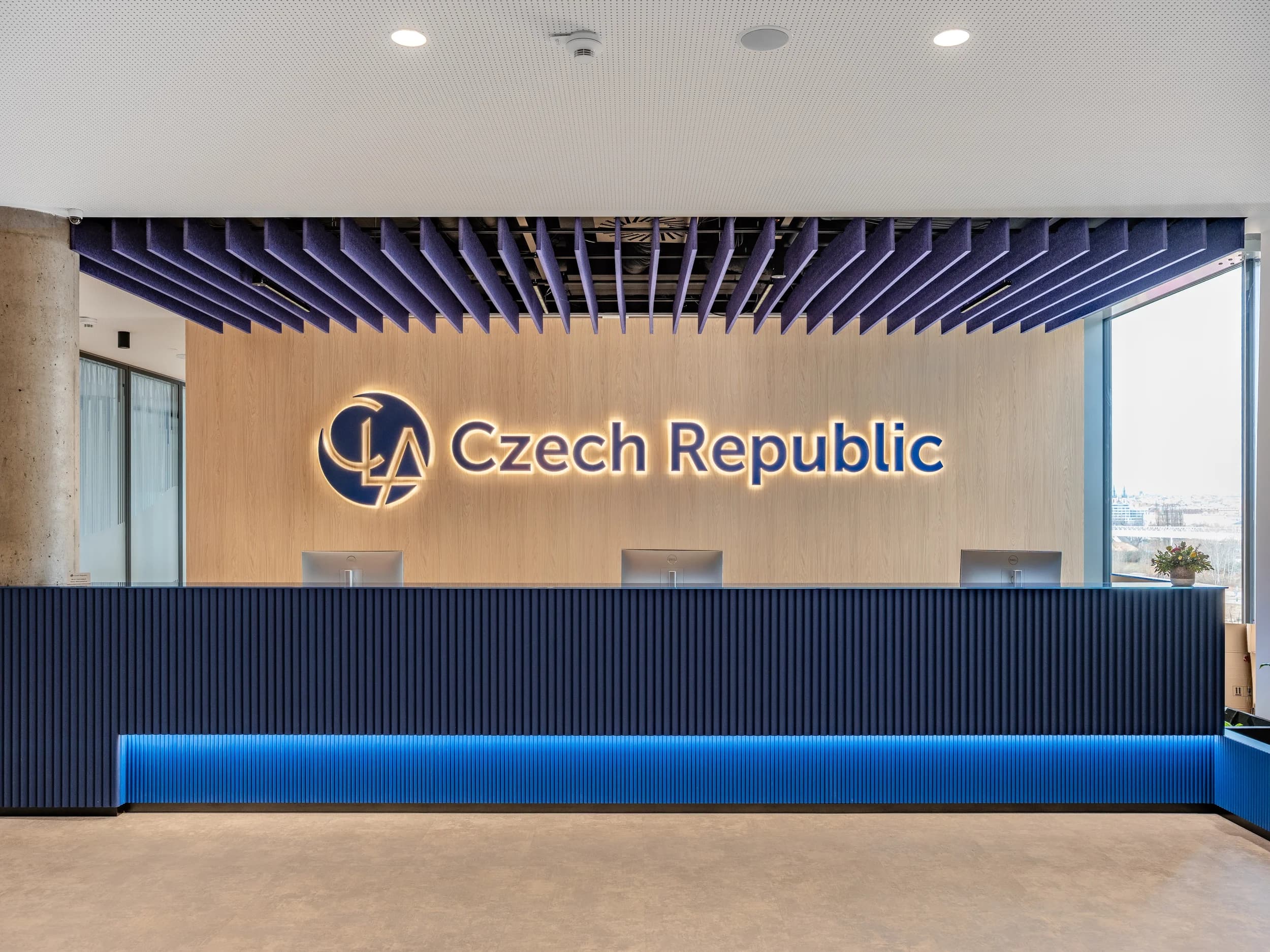 Recepce CLA Czech Republic v Praze s tmavě modrým pultem a podsvíceným logem na dřevěné stěně
