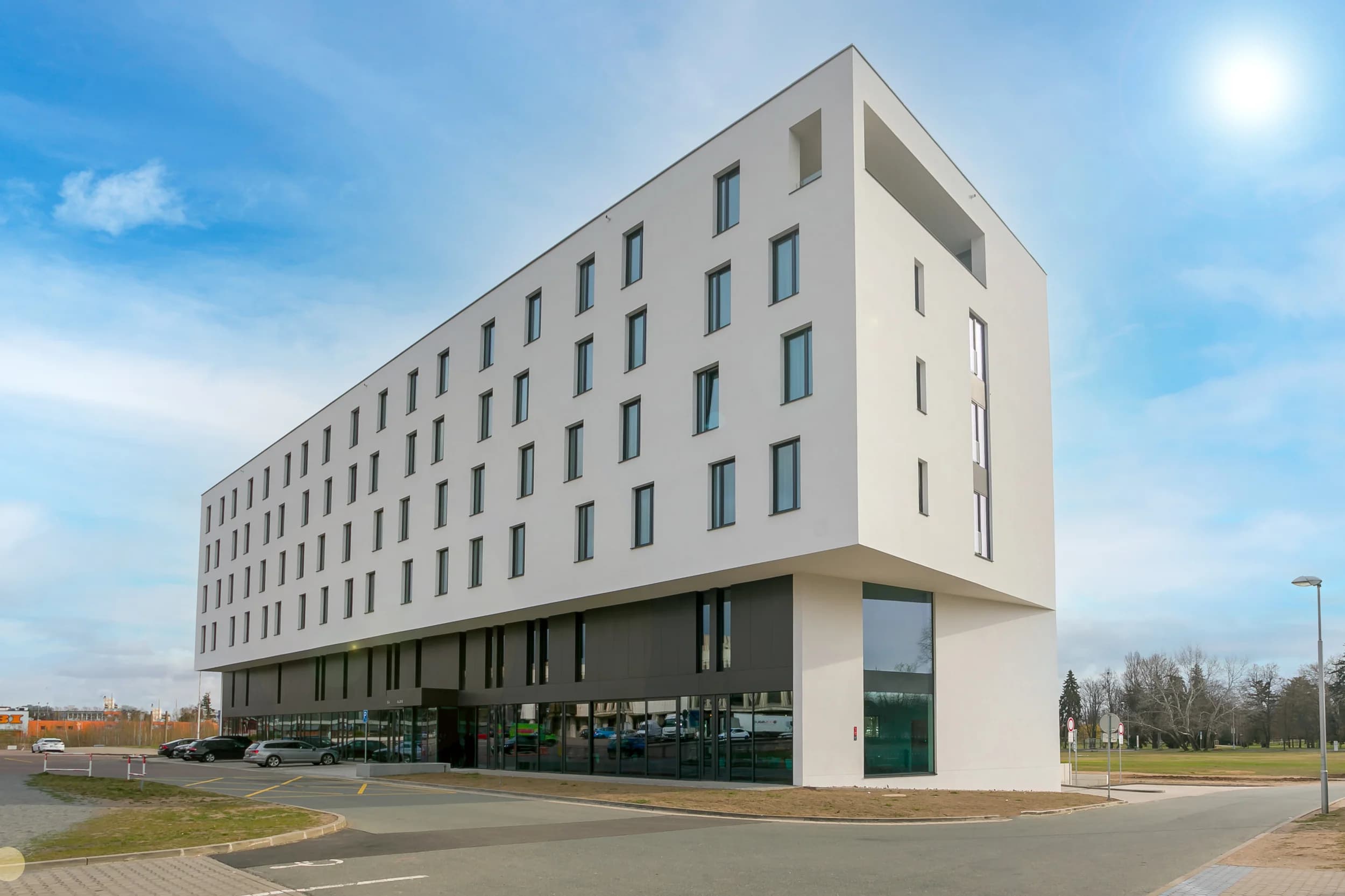 Moderní bílá budova Hotelu Aldis v Hradci Králové s proskleným přízemím a parkovištěm